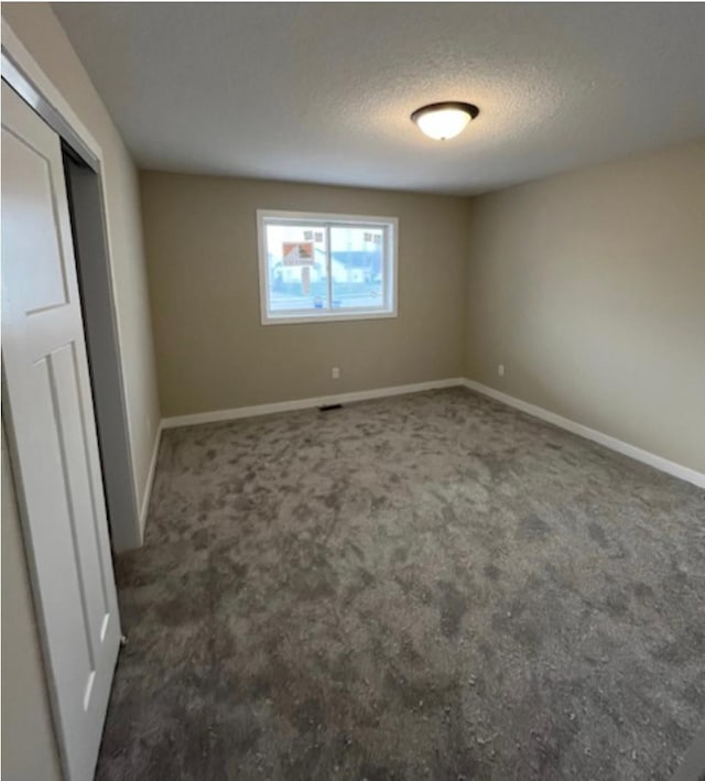 unfurnished bedroom featuring a textured ceiling and dark carpet