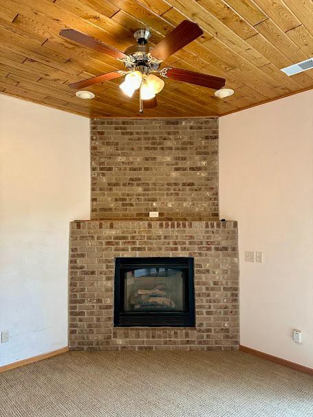 unfurnished living room with carpet flooring, ceiling fan, wooden ceiling, and a fireplace