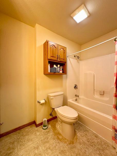 bathroom with shower / tub combo with curtain, tile patterned flooring, and toilet