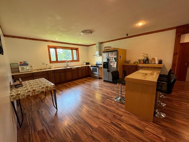 kitchen featuring hardwood / wood-style floors, appliances with stainless steel finishes, kitchen peninsula, and wall chimney exhaust hood