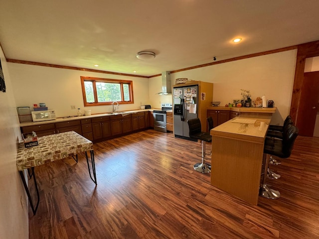 kitchen featuring dark wood-type flooring, ornamental molding, a kitchen breakfast bar, stainless steel appliances, and wall chimney exhaust hood