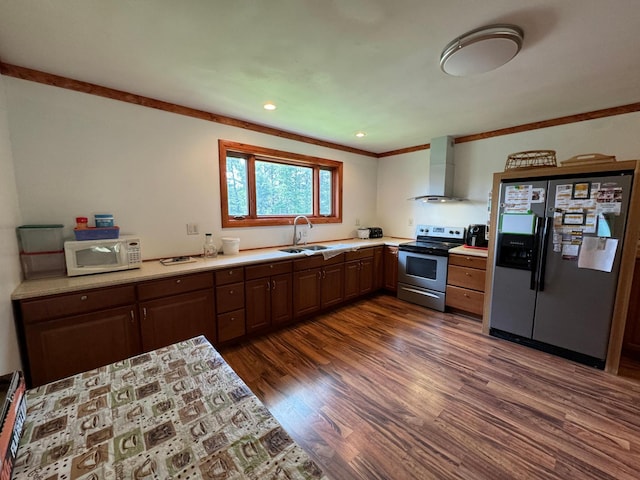 kitchen with a sink, dark wood finished floors, stainless steel appliances, wall chimney exhaust hood, and light countertops