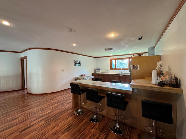 kitchen featuring crown molding, dark wood-style flooring, a peninsula, a kitchen breakfast bar, and a sink