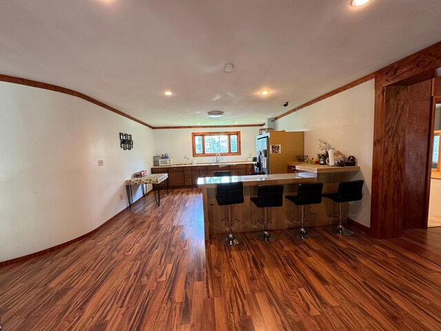 kitchen with a breakfast bar, sink, kitchen peninsula, crown molding, and dark hardwood / wood-style flooring