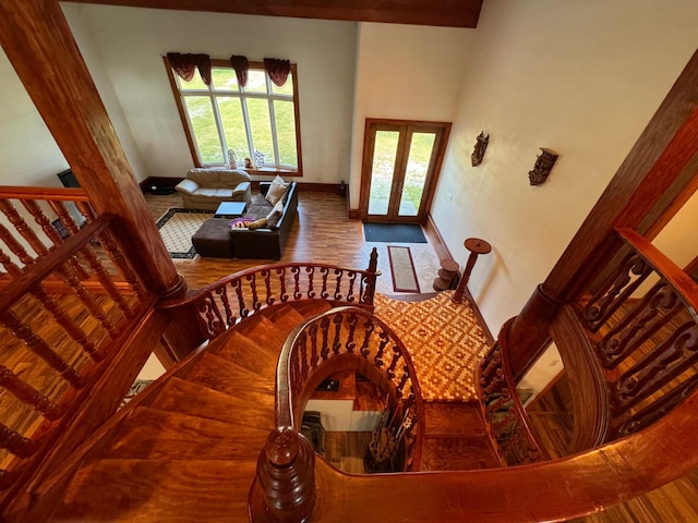 staircase with french doors, a high ceiling, baseboards, and wood finished floors