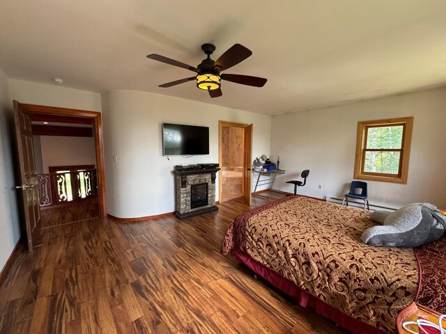 unfurnished bedroom with a stone fireplace, ceiling fan, hardwood / wood-style flooring, and baseboard heating