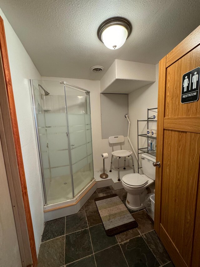 bathroom with tile patterned floors, toilet, a shower with door, and a textured ceiling