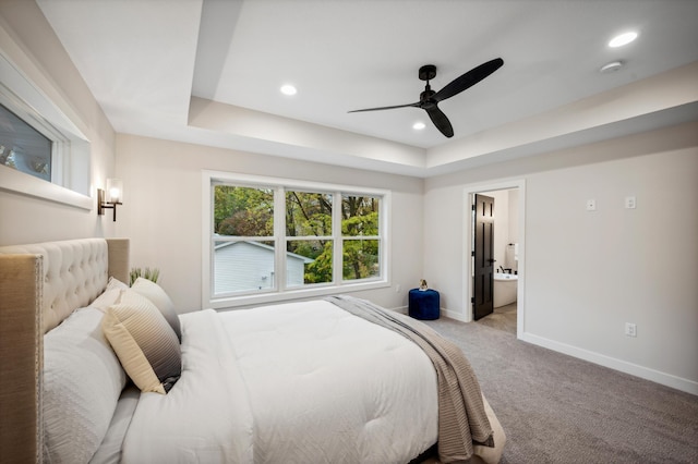 bedroom featuring ceiling fan, a raised ceiling, light colored carpet, and ensuite bath