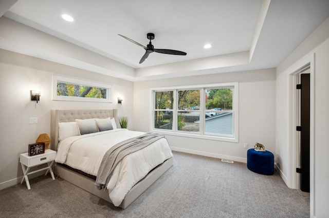 carpeted bedroom featuring ceiling fan and a raised ceiling