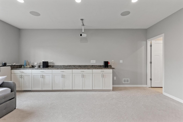bar with light colored carpet, white cabinetry, and dark stone counters