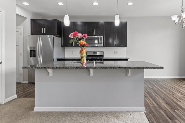 kitchen with stainless steel appliances, a kitchen island with sink, carpet flooring, and pendant lighting
