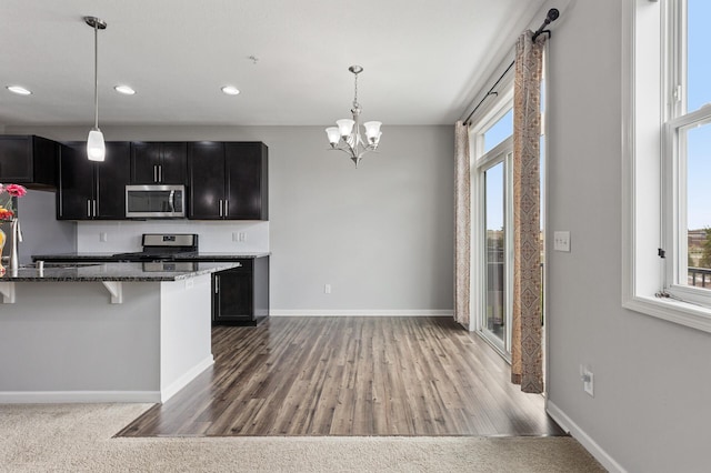 kitchen with decorative light fixtures, stone countertops, a breakfast bar area, wood-type flooring, and appliances with stainless steel finishes