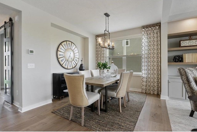 dining space with a barn door, light hardwood / wood-style flooring, and a notable chandelier