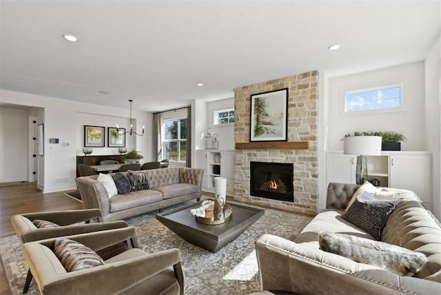 living room featuring hardwood / wood-style floors, an inviting chandelier, and a stone fireplace