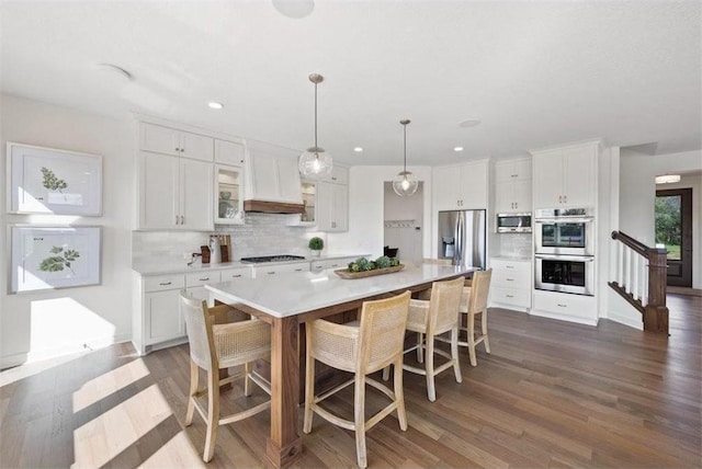 kitchen with decorative backsplash, appliances with stainless steel finishes, white cabinets, a kitchen island, and hanging light fixtures