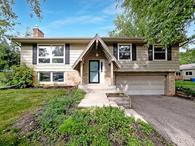 split foyer home with a garage, a chimney, aphalt driveway, and brick siding