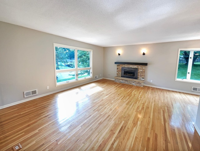 unfurnished living room with a healthy amount of sunlight, a brick fireplace, light wood-type flooring, and visible vents