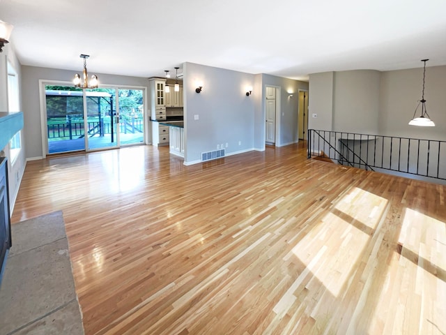 unfurnished living room featuring a chandelier, baseboards, visible vents, and light wood finished floors