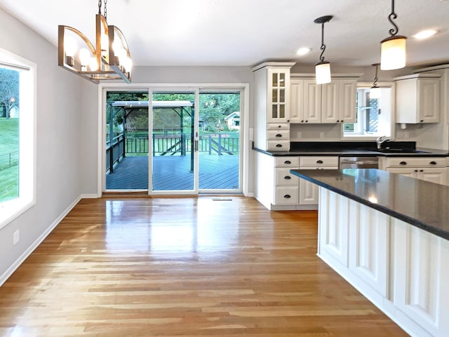 kitchen with hanging light fixtures, dark countertops, glass insert cabinets, and white cabinetry