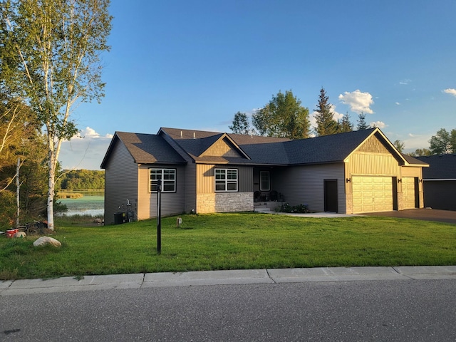 view of front of house with an attached garage, a water view, stone siding, driveway, and a front lawn