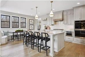 kitchen with a kitchen bar, light hardwood / wood-style floors, stainless steel double oven, an island with sink, and pendant lighting