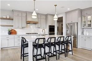 kitchen with appliances with stainless steel finishes, light hardwood / wood-style flooring, tasteful backsplash, and a kitchen island with sink