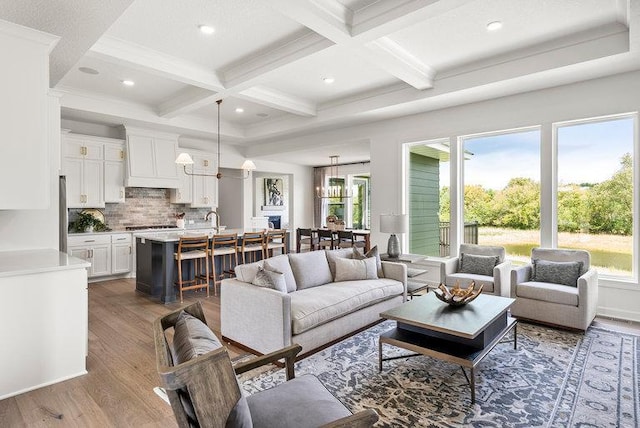 living room featuring hardwood / wood-style flooring, coffered ceiling, beamed ceiling, sink, and a notable chandelier