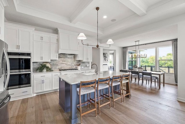 kitchen with decorative light fixtures, a center island with sink, wood-type flooring, custom exhaust hood, and beamed ceiling