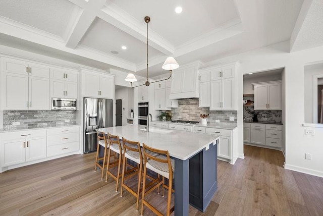 kitchen featuring hardwood / wood-style flooring, tasteful backsplash, appliances with stainless steel finishes, and a center island with sink