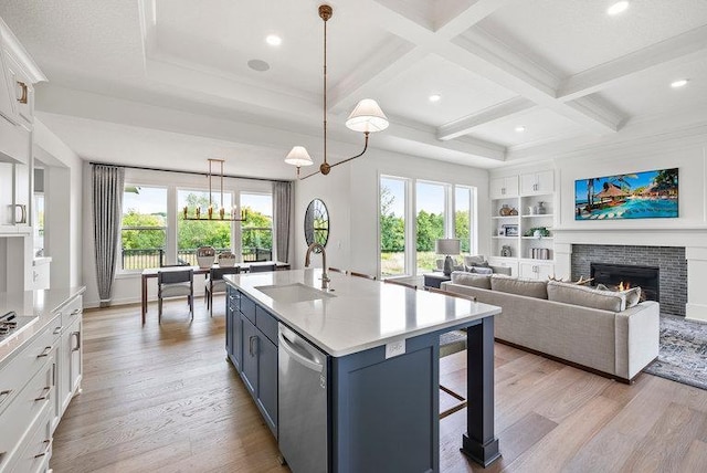 kitchen with coffered ceiling, white cabinets, light hardwood / wood-style floors, stainless steel dishwasher, and a kitchen island with sink