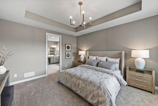 bedroom with carpet floors, a notable chandelier, a tray ceiling, and ensuite bathroom