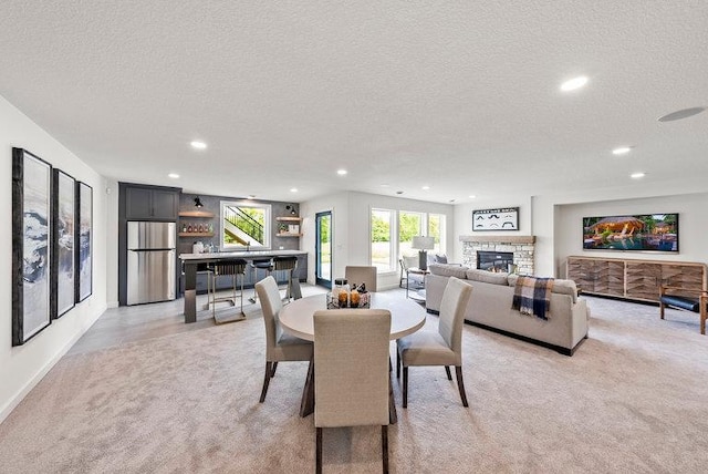 carpeted dining area featuring a stone fireplace, a wealth of natural light, and a textured ceiling