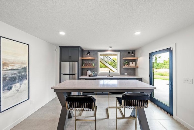 kitchen with a center island, a breakfast bar, stainless steel refrigerator, sink, and a textured ceiling