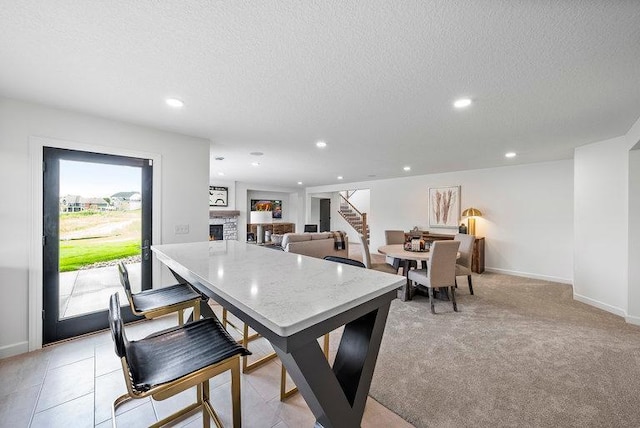 carpeted dining room featuring a stone fireplace and a textured ceiling