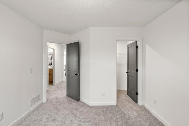 unfurnished bedroom with a closet, a textured ceiling, a walk in closet, and light carpet