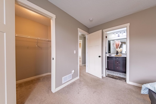 unfurnished bedroom with a closet, a textured ceiling, light carpet, connected bathroom, and a walk in closet