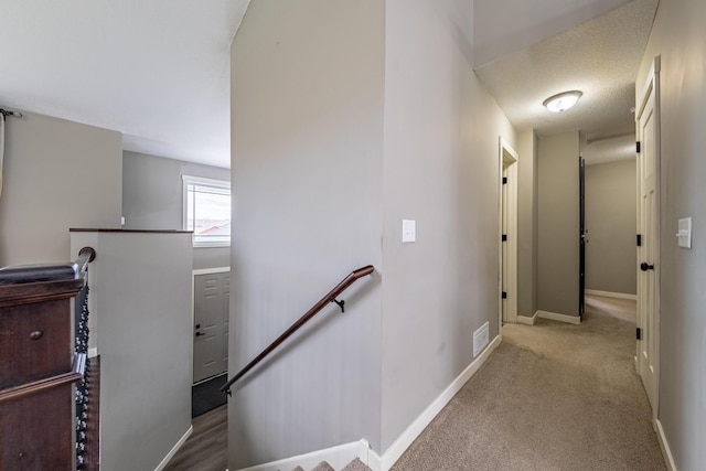 corridor with a textured ceiling and light colored carpet