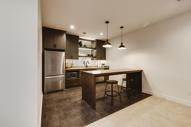 kitchen with sink, built in microwave, decorative light fixtures, a breakfast bar area, and stainless steel refrigerator