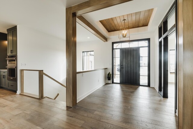 foyer with a raised ceiling, an inviting chandelier, light hardwood / wood-style flooring, and wooden ceiling