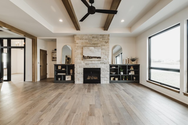 unfurnished living room featuring a stone fireplace, ceiling fan, a tray ceiling, beamed ceiling, and wood-type flooring