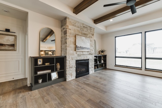 living room featuring beam ceiling, ceiling fan, a fireplace, and wood-type flooring