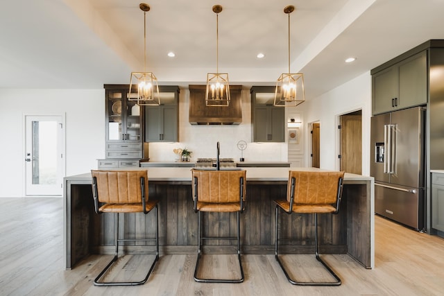 kitchen featuring hanging light fixtures, a kitchen breakfast bar, an island with sink, light hardwood / wood-style floors, and high end fridge