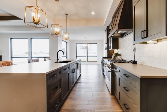 kitchen featuring pendant lighting, a large island with sink, sink, stainless steel stove, and custom range hood