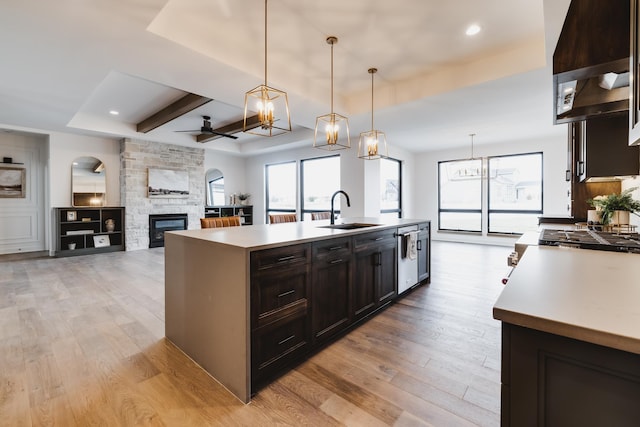 kitchen featuring a kitchen island with sink, a stone fireplace, sink, decorative light fixtures, and light hardwood / wood-style floors