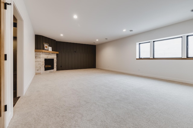 unfurnished living room featuring a stone fireplace and light colored carpet