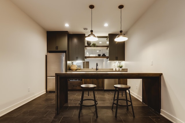 bar with dark brown cabinetry, stainless steel refrigerator, hanging light fixtures, and sink