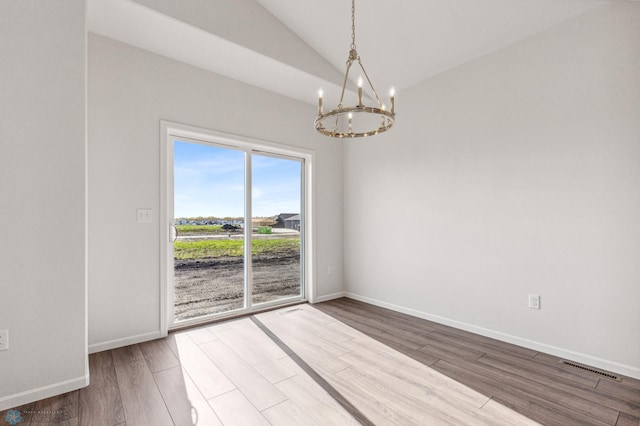 empty room with vaulted ceiling, hardwood / wood-style floors, and a chandelier