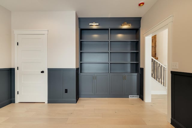 interior space featuring light wood-style floors, a decorative wall, and wainscoting