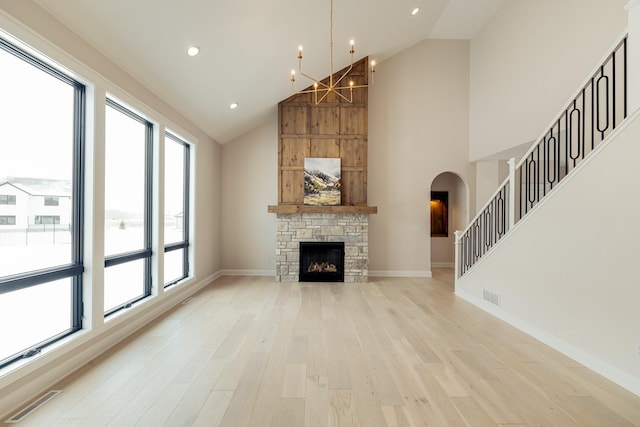 unfurnished living room with baseboards, visible vents, a stone fireplace, light wood-style floors, and high vaulted ceiling