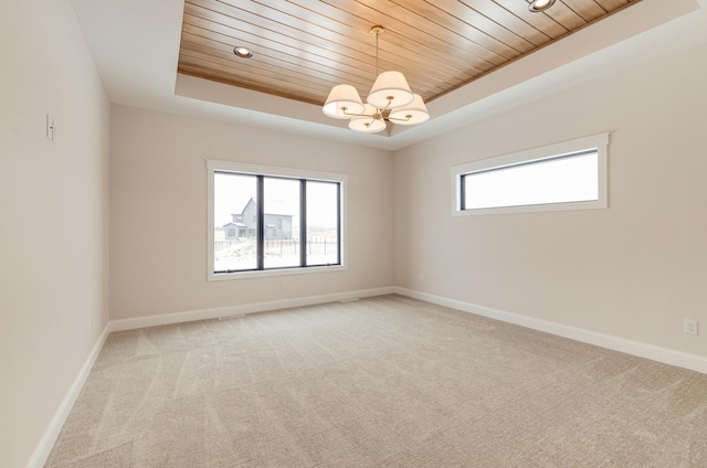 unfurnished room featuring wooden ceiling, light colored carpet, baseboards, a tray ceiling, and an inviting chandelier